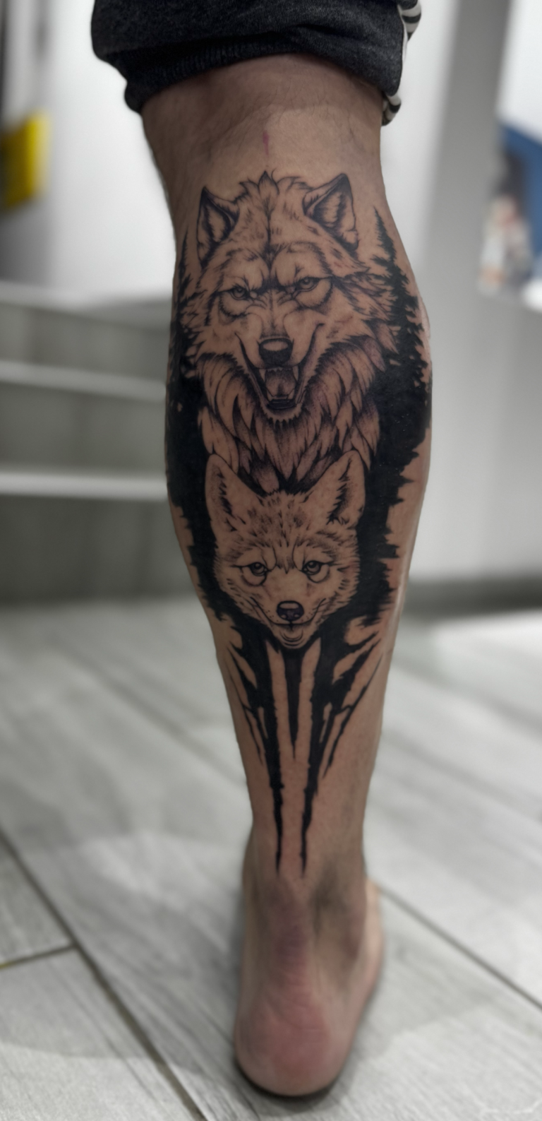 Tatouage noir et gris de deux loups sur le mollet, avec aplats sombres et effet de coulures