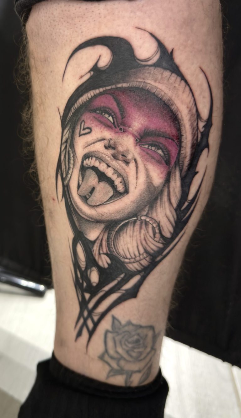 Tatouage portrait expressif noir et gris avec accents rouges/roses sur la jambe